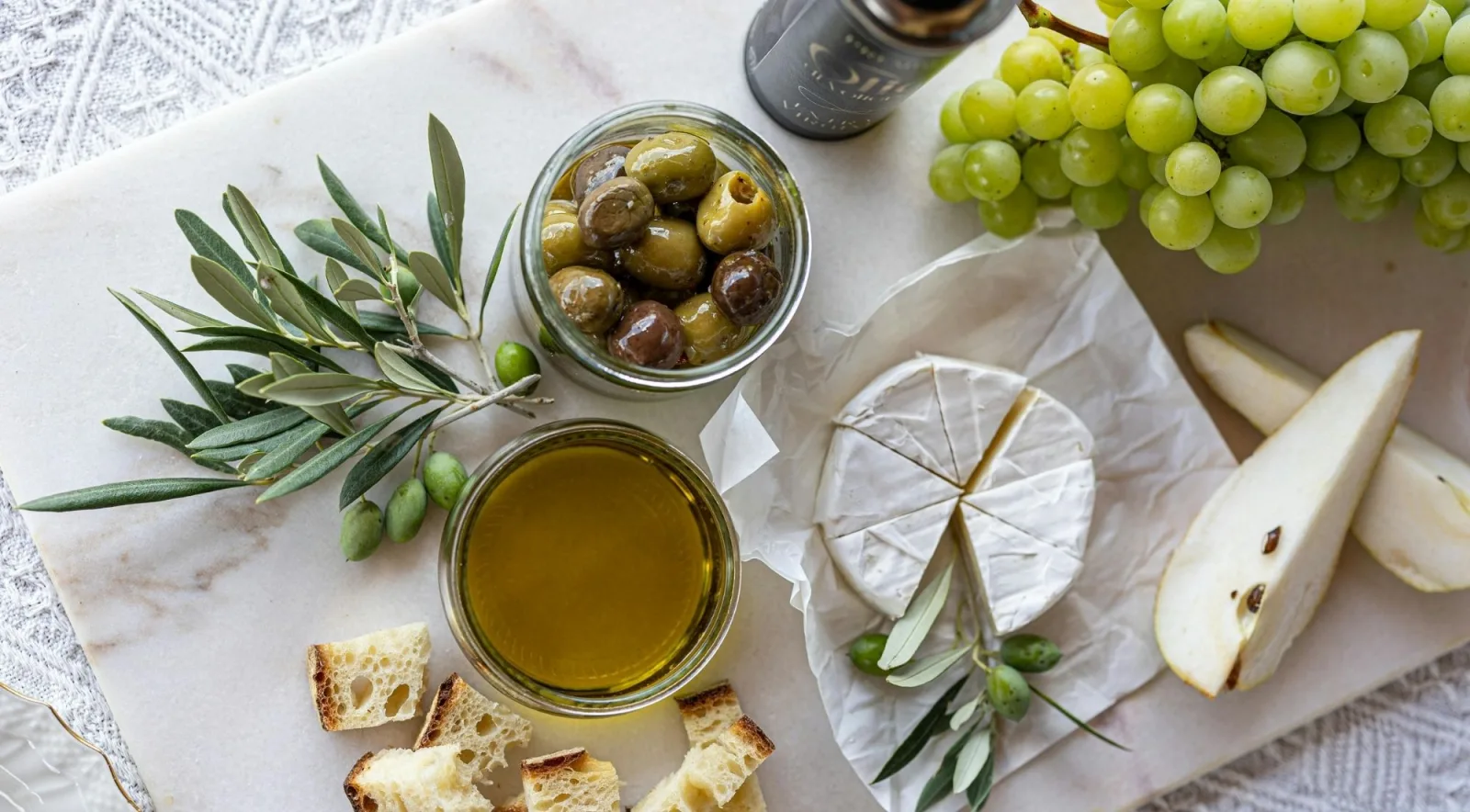 Olive oil, olives, soft cheese, bread and grapes laid out for a tasting